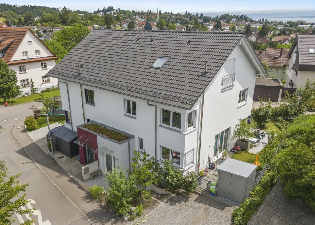 Moderne mehrstöckige Doppelhaushälfte mit Garten und Terrasse in einem grünen Wohngebiet an einem sonnigen Tag.