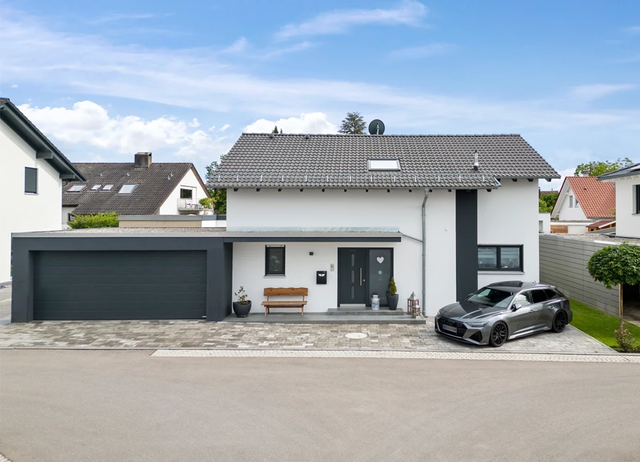 Modernes Einfamilienhaus mit stilvoller weiß-grauer Fassade. In der Einfahrt seht ein graues Auto neben einem gepflegten Vorgarten.