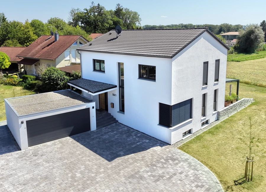 Modernes Einfamilienhaus mit Doppelgarage, umgeben von Grünflächen und Nachbarhäusern an einem sonnigen Tag.