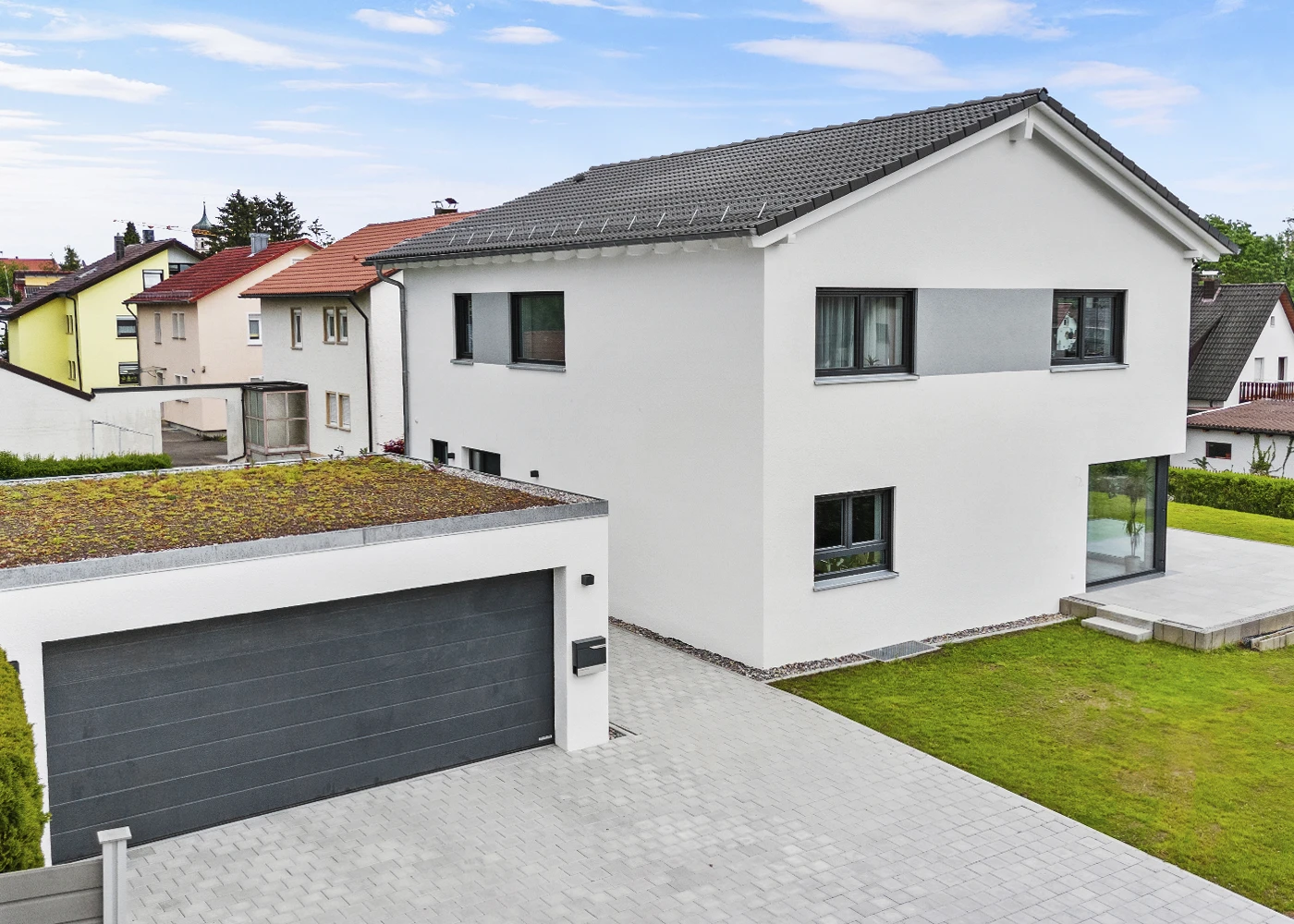 Modernes Einfamilienhaus mit Garage und begrüntem Dach in einer Wohnsiedlung, umgeben von gepflegtem Garten.