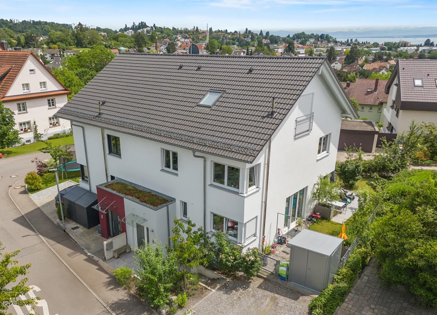 Moderne mehrstöckige Doppelhaushälfte mit Garten und Terrasse in einem grünen Wohngebiet an einem sonnigen Tag.