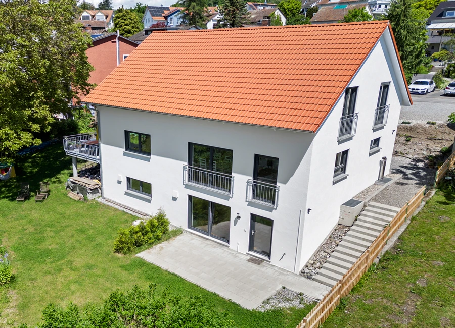 Modernes Einfamilienhaus mit leichter Hanglage, rotem Dach und Garten an sonnigem Tag, umgeben von einem schönen grün angelegten Garten.