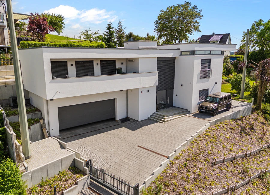 Sehr moderne weiße Villa mit Flachdach, einem Garagenzugang und geparktem Auto im Vordergrund.