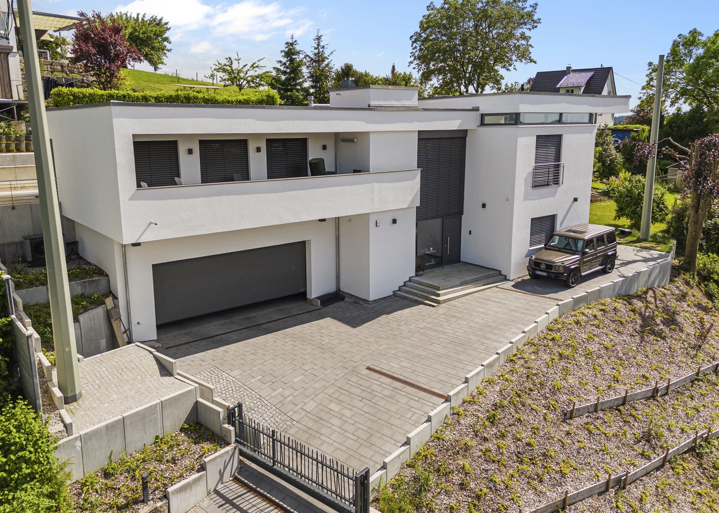 Sehr moderne weiße Villa mit Flachdach, einem Garagenzugang und geparktem Auto im Vordergrund.