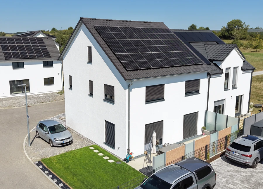 Zweistöckiges modernes Haus mit Solaranlagen auf dem Dach, umweltfreundliche Energie in Wohnsiedlung, sonniger Tag.