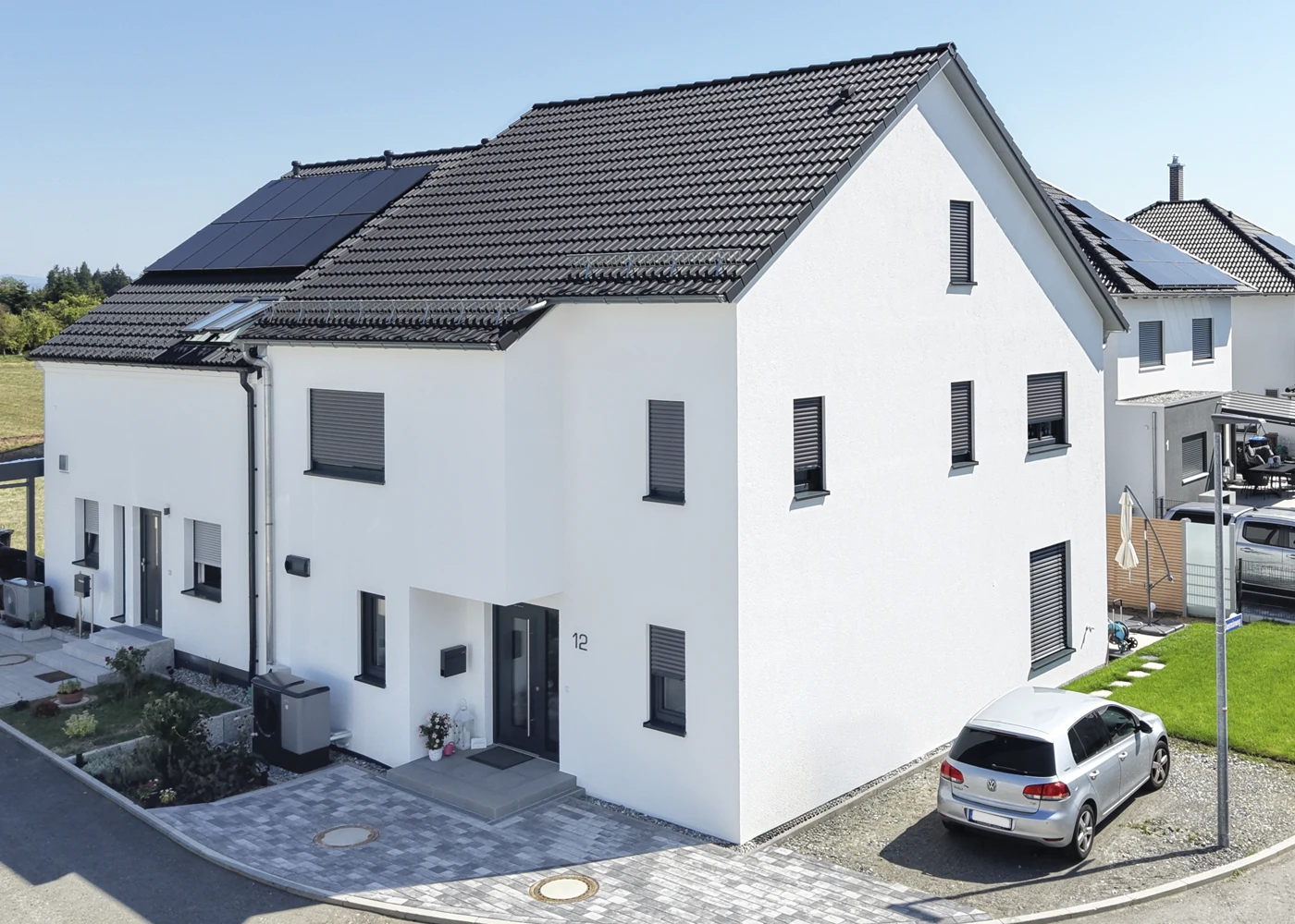 Moderne, Doppelhaushälfte und kleinem Garten. Ein Auto steht auf dem Grundstück, sonniger Tag im Wohnviertel.