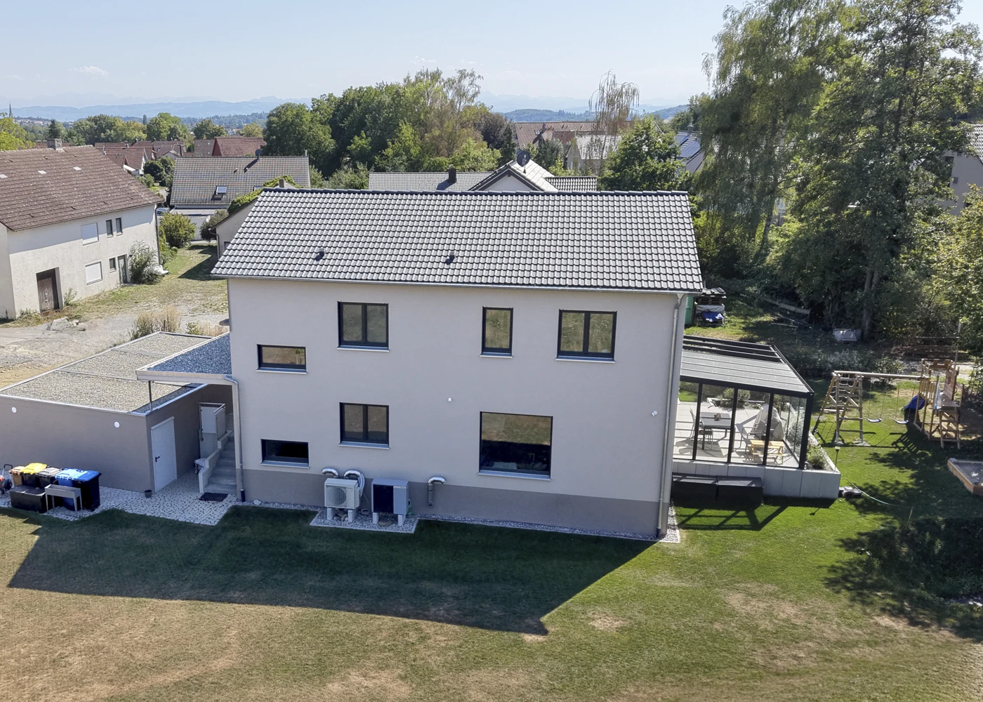 Zweistöckiges modernes Haus mit großem Garten und Wintergarten in ruhiger Wohngegend bei Sonnenschein.