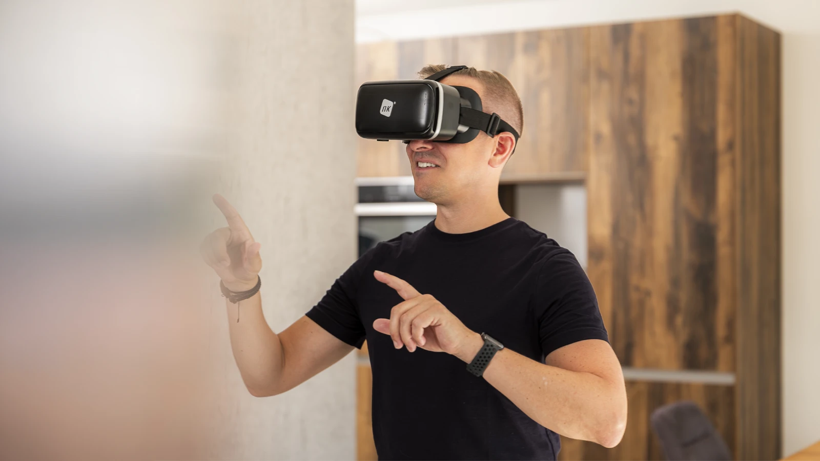 Person mit VR-Brille erlebt virtuelle Realität, zeigt auf unsichtbare Elemente in einem modernen Raum.